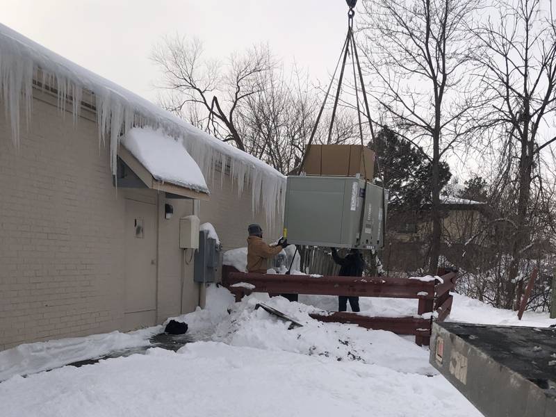 Crew guiding a rooftop unit in the snow